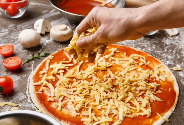 Man adding cheese on pizza base