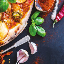 tasty pizza on a black background with spices and vegetables